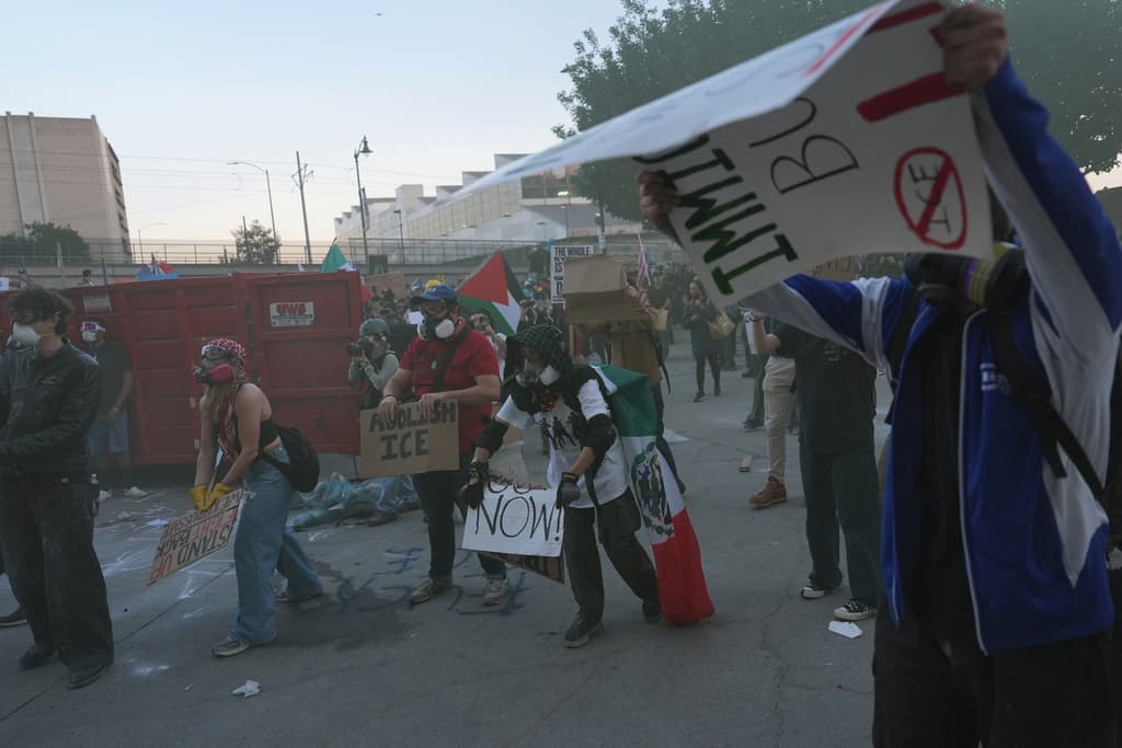 Manifestantes agitan sus pancartas para intentar disipar el gas lacrimógeno disparado por la policía federal en el Centro de Detención Metropolitano del centro de Los Ángeles.