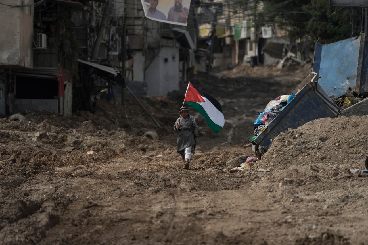 El activista palestino Khairi Hanoon camina con la bandera de Palestina en medio de un camino arruinado luego del paso de las
<a href="https://www.univision.com/noticias/mundo/israel-guerra-en-gaza-transformacion-de-israel-en-un-estado-paria-analisis-luciano-zaccara">tropas israelíes en Tulkarem, Cisjordania,</a> en septiembre de 2024. La violencia de la guerra en Gaza se extendió por el otro territorio palestino ocupado, que no está gobernado por Hamas, sino por la Autoridad Palestina.