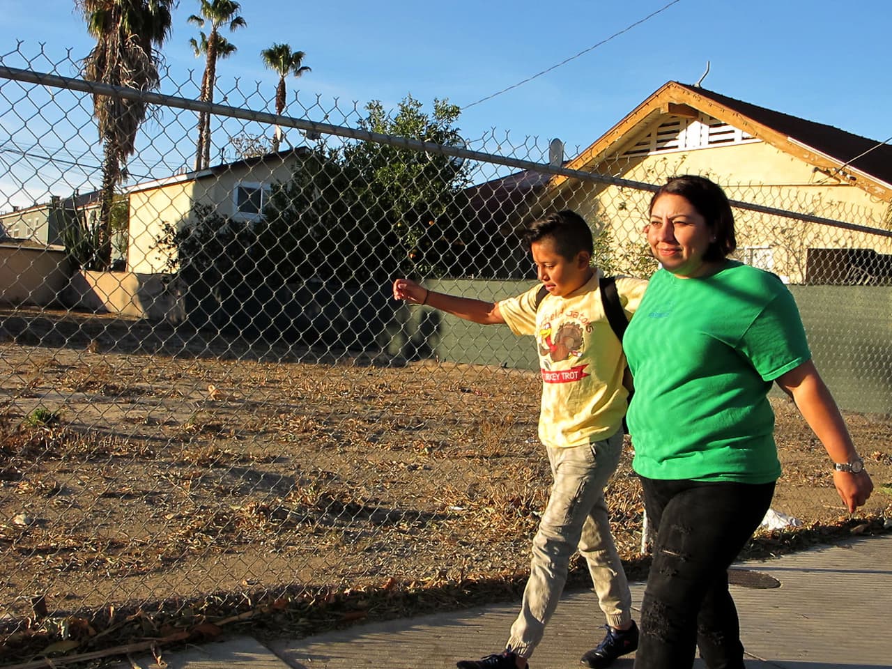 Idalia Ríos, una madre y vecina activista, camina a la escuela con su hijo Andrew, de 10 años, a través del vecindario Lacy de Santa Ana, en 2018. El lote baldío a sus espaldas, un área preocupante en una zona con contaminación por plomo, fue luego convertido por la ciudad en un parque, luego que activistas presionaran por más espacios al aire libre.