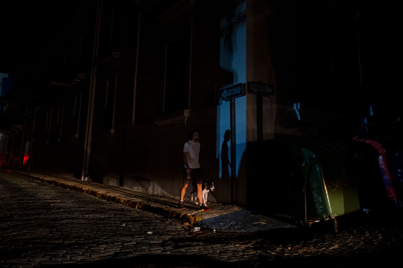Un hombre pasea a su perro en una calle que quedó a oscuras por un corte de energía en el Viejo San Juan, Puerto Rico.