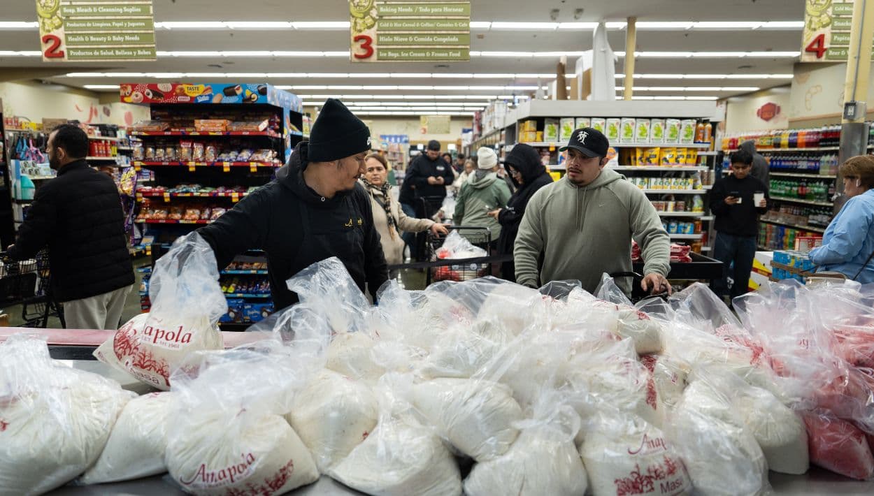 Alex Díaz, a la izquierda, toma una bolsa de malas para hacer tamales, mientras otros coladores esperan en fila en el mercado Amapola en Downey, California el martes 23 de diciembre