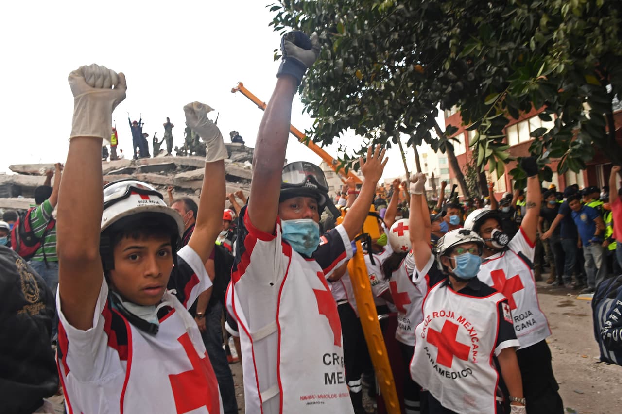 A group of Mexican Red Cross rescuers indicate that it is time to remain silent. The slightest sound guides the experts to the presence of survivors who might still be in the rubble.