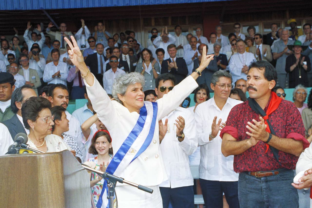 Daniel Ortega applauds after placing the presidential sash on his opponent Violeta Barrios de Chamorro, in Managua, April 25, 1990. Chamorro pulled off an upset by defeating the Sandinista leader in elections.