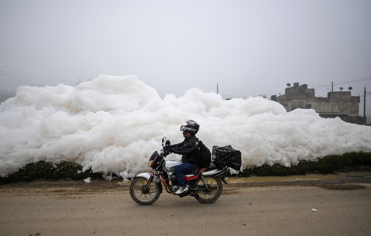 Un motociclista pasa por la espuma que invadió el barrio Los Puentes, en Mosquera.
<br>
<br>"Esto es producto de la contaminación, de la mala disposición de los residuos, materiales, animales muertos, basura, grasas y detergentes", explica a la AFP Sergio Valero, director de gestión del riesgo de Mosquera, municipio de la cuenca baja del rio Bogotá.
<br>