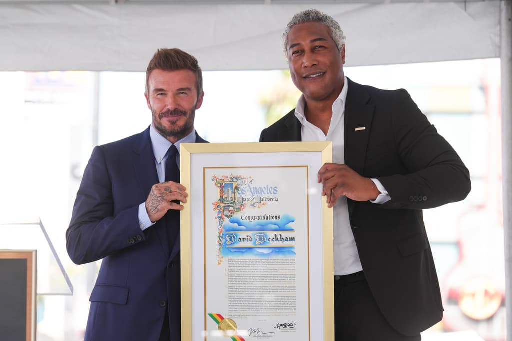 Conforme el evento tomó forma, Beckham continuó el recorrido protocolario acompañado por organizadores e invitados vinculados al acto. El registro captó saludos y momentos de transición previos a los discursos, cuando la ceremonia todavía se movía entre lo formal y lo cercano, con el público siguiendo cada paso detrás de las vallas. En la foto: David Beckham (izquierda) y Ron Frierson.