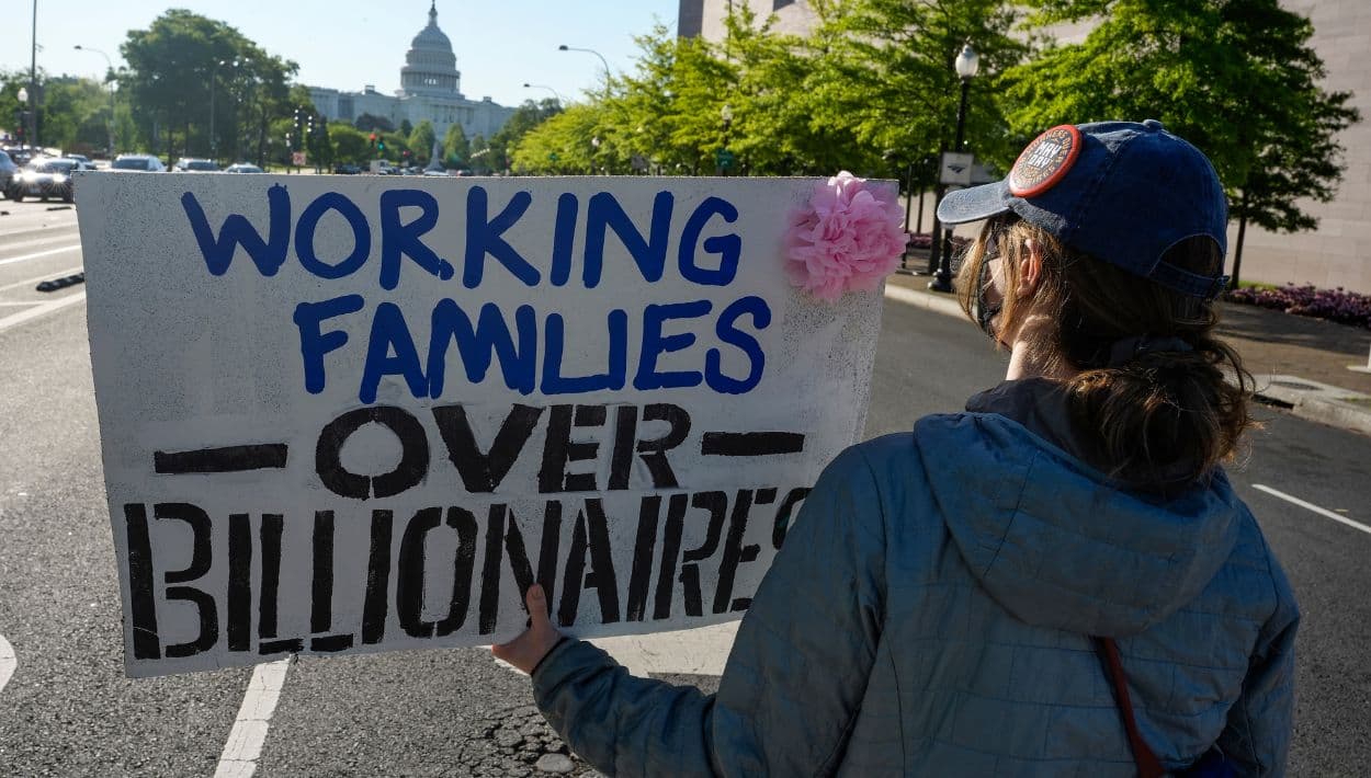 "Las familias trabajadoras por encima de los multimillonarios" expresa otro cartel durante la marcha para conmemorar el Día Internacional de los Trabajadores, donde activistas protestan lo que llaman una toma del gobierno por parte de los multimillonarios.